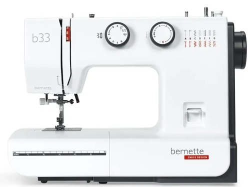Maszyna do szycia BERNETTE B33 w kolorze białym, z 15 ściegami. Widoczny mechanizm, dwa pokrętła do regulacji, jedno z logo bernette. Z przodu umieszczony jest wskaźnik długości ściegu. Urządzenie stojące, z otwartą przestrzenią roboczą.