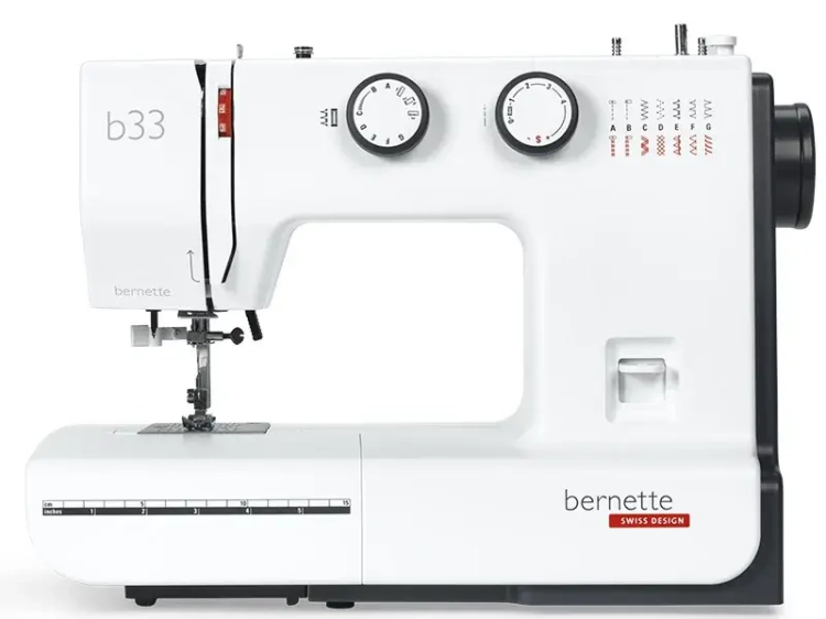 Maszyna do szycia BERNETTE B33 w kolorze białym, z 15 ściegami. Widoczny mechanizm, dwa pokrętła do regulacji, jedno z logo bernette. Z przodu umieszczony jest wskaźnik długości ściegu. Urządzenie stojące, z otwartą przestrzenią roboczą.