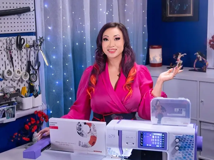 Maszyno-hafciarka BERNETTE B79 SE Yaya Han w kolorze białym i niebieskim, z wyświetlaczem dotykowym, stoi na stole. Obok widoczna instrukcja oraz akcesoria. Tło z dekoracjami i narzędziami krawieckimi. Produkt prezentowany w aranżacji krawieckiej.
