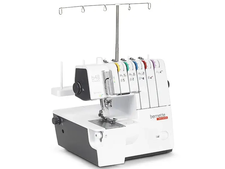Coverlok Bernette B48 Funlock to overlock w kolorze białym i czarnym, z pięcioma szpulami w różnych kolorach. Widoczna igła oraz stół do szycia. Maszyna stoi w pozycji pionowej, z wysuwaną belką do nawlekania nici. W komplecie gratis.