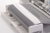 Ploter tnący Silhouette Cameo 4 w kolorze białym, z widoczną rolką błyszczącego, srebrnego materiału. Ujęcie z boku, pokazujące otwarte podajnik i elementy robocze urządzenia. Proste tło, które podkreśla detale maszyny.