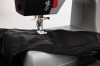 Maszyna do szycia Veritas Power Stitch PRO w zbliżeniu, z igłą i stopką na czarnej skórzanej tkaninie. Widoczny mechanizm oraz elementy kontrolne na obudowie. Ujęcie z boku, ukazujące detale szycia.