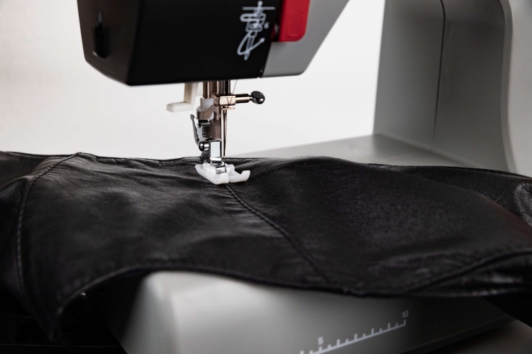 Maszyna do szycia Veritas Power Stitch PRO w zbliżeniu, z igłą i stopką na czarnej skórzanej tkaninie. Widoczny mechanizm oraz elementy kontrolne na obudowie. Ujęcie z boku, ukazujące detale szycia.