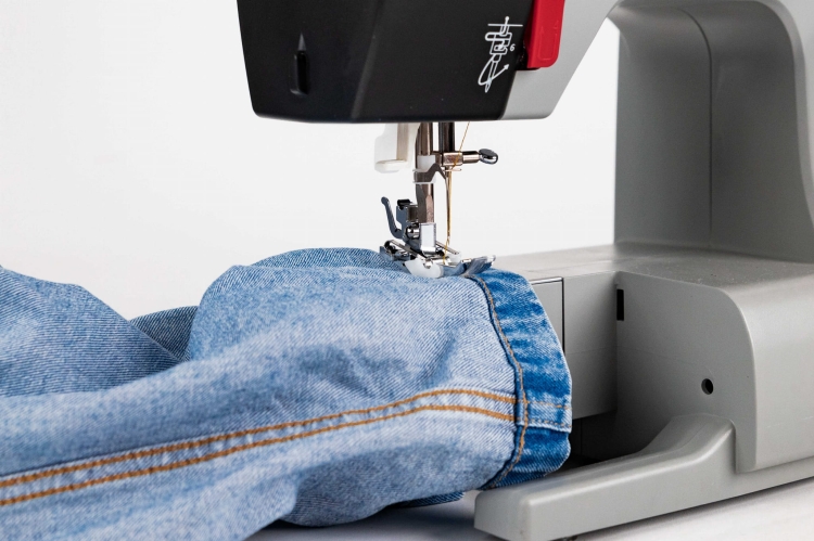 Maszyna do szycia Veritas Power Stitch PRO z widocznym elementem szyjącym, umieszczona na blacie. Na zdjęciu widać fragment denimu z żółtą nicią przeszywającą krawędź materiału. Ujęcie z bliska, pokazujące szczegóły mechanizmu i materiału.