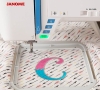 Maszyno-hafciarka Janome Skyline S9 z programem Artistic Digitizer JR. Widok z bliska na kolorową aplikację litery C w ramce hafciarskiej, z włączonym przyciskiem START i wyraźnymi przyciskami na obudowie maszyny. Tło w wzory strzałek.