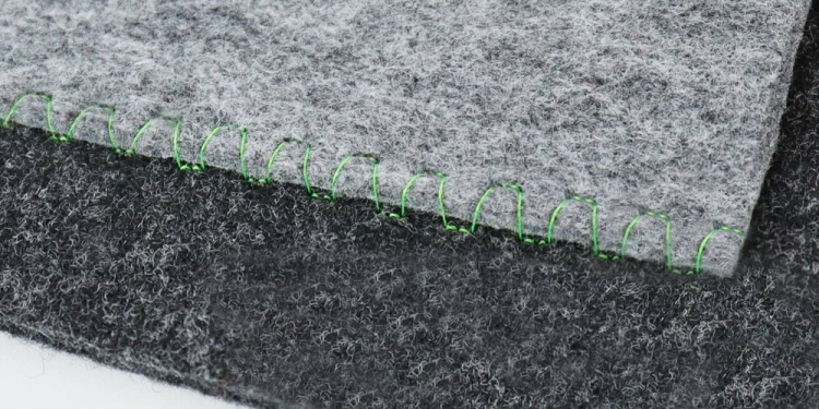 Maszyna do szycia Janome HD 523 EASY JEANS, pokazana na tle dwóch kawałków filcu w odcieniach szarości, z widocznym zielonym ściegiem. Ujęcie z góry, ukazujące detale szycia oraz teksturę materiału.