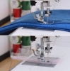Maszyna do szycia Janome HD 523 EASY JEANS, w ujęciu z bliska, pokazuje stopkę z igłą, szyjącą gruby materiał dżinsowy oraz siateczkę, z widocznym czerwonym nitką. W tle szpulki nici w różnych kolorach.