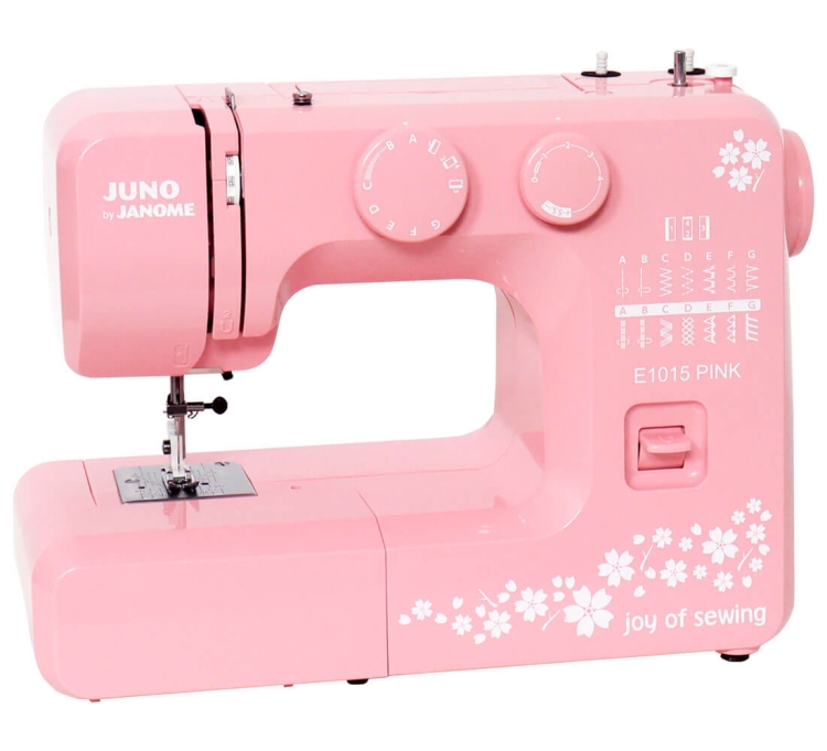 Maszyna do szycia Janome JUNO E1015 w kolorze różowym, z widocznymi pokrętłami do ustawiania ściegów i ozdobnym nadrukiem kwiatowym. Ujęcie frontalne, ukazujące stół maszyny i igłę w pozycji roboczej.