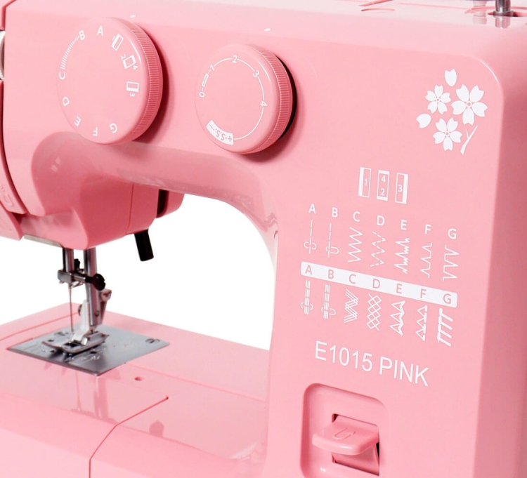 Maszyna do szycia Janome JUNO E1015 PINK w kolorze różowym. Widoczne pokrętła do ustawiania ściegów oraz instrukcje na obudowie. Na froncie znajduje się logo E1015 PINK oraz wzory ściegów. Ujęcie z boku, ukazujące detale i funkcje maszyny.
