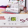 Maszyna do szycia Janome JUNO E1030 w kolorze białym z dekoracyjnymi kwiatami. Wyposażona w wyświetlacz LED, 30 programów szycia. Wymiary: 38 cm (szerokość), 28 cm (wysokość), 16 cm (głębokość). Widoczny zestaw igieł Janome obok.