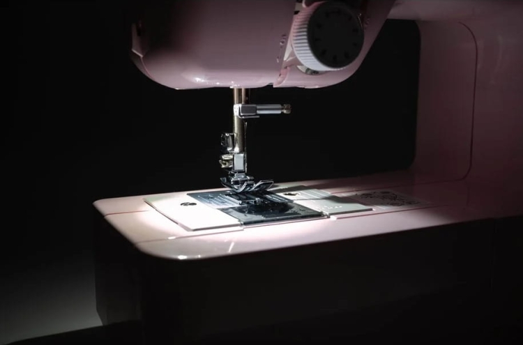 Maszyna do szycia Brother LP14 Pink Limited Edition w kolorze różowym, z widoczną stopką i czarną nicią na materiale. Ujęcie z boku, ukazujące detale mechanizmu oraz panel sterujący, w ciemnym tle.
