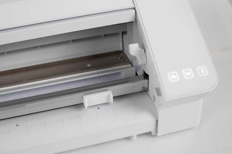 Ploter Silhouette Cameo 4 Pro w kolorze białym, widok z góry na otwarte wnętrze, z widocznym metalowym prowadnikiem i przyciskami sterującymi. Zawiera oznaczenia do ustawienia materiału oraz port do podłączenia.
