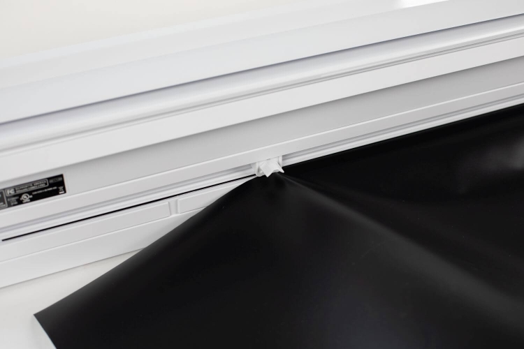 Ploter Silhouette Cameo 4 Pro w kolorze białym z widocznym nawiniętym czarnym materiałem. Ujęcie z boku, pokazujące detal wprowadzenia materiału do urządzenia, z widoczną etykietą z informacjami technicznymi.