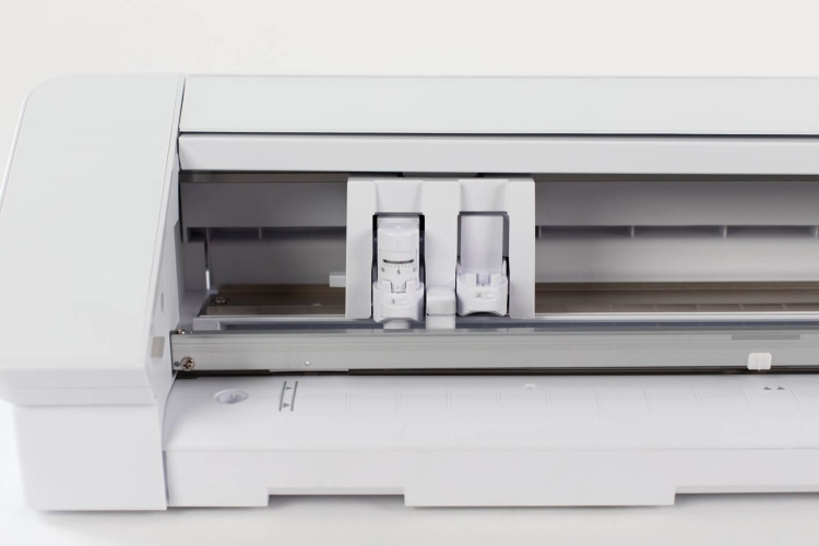Ploter Silhouette Cameo 4 Pro w kolorze białym, z widocznymi dwoma głowicami tnącymi umieszczonymi w przedniej części. Ujęcie z przodu, pokazujące wnętrze maszyny oraz prowadnice tnące na dolnej części. Prosty, jasny kontekst na białym tle.