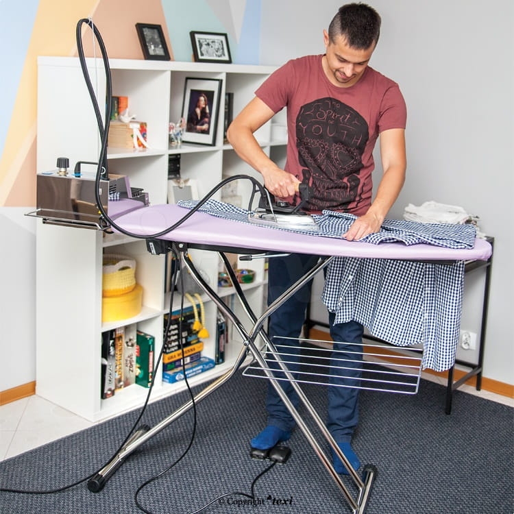 Stół prasowalniczy TEXI CHAMPION SB z nadmuchem i odsysaniem, w kolorze fioletowym, z osobą prasującą koszulę. Widoczny element odsysający oraz półka na prasowane ubrania w dolnej części. Ujęcie frontalne, stół ustawiony w domowym wnętrzu.
