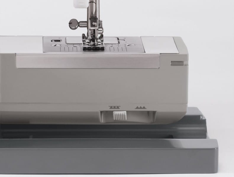 Maszyna do szycia Singer 4411 Heavy Duty w kolorze szarym, z metalową stopką i widoczną igłą. Ujęcie frontalne pokazuje panel roboczy oraz pokrętło regulacji. Produkt umieszczony na ciemnoszarym podłożu, z prostym, jasnym tłem.